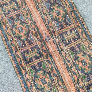Op de afbeelding: Een rechthoekig loperkleed met een herhalend geometrisch en bloemmotief in tinten terracotta oranje, diep marineblauw en bosgroen. Het ontwerp bestaat uit verticale banen met ingewikkelde motieven en een centraal geweven textuur.