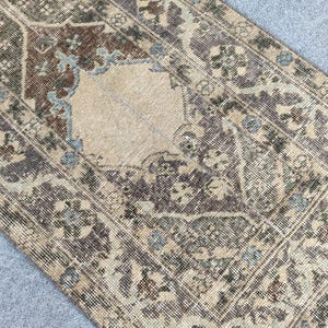 Könnte beinhalten: Ein Teppich im antiken Stil mit einem beigen Mittelmedaillon und einem Rand mit floralen und geometrischen Mustern. Der Teppich hat einen Used-Look mit Braun-, Beige- und Blautönen.