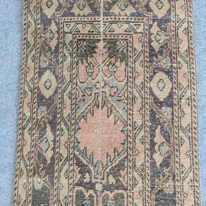 Peut inclure: Un tapis rectangulaire vintage avec un motif floral central dans des tons pêche, verts et bleus. Le tapis présente une bordure marron foncé avec des motifs géométriques et des losanges. L'aspect vieilli du tapis suggère qu'il s'agit d'une antiquité.