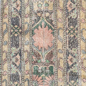 Pode incluir: Um tapete retangular em estilo vintage com um design floral central em tons de pêssego e verde. O tapete apresenta um padrão repetitivo de listras verticais em preto, bege e pêssego, criando um visual desgastado e antigo. O design do tapete é detalhado e intrincado.