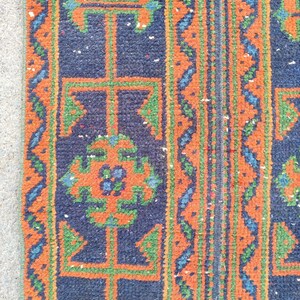 Könnte beinhalten: Nahaufnahme eines Teppichabschnitts mit dunkelblauem Hintergrund und geometrischen Mustern in Orange, Grün und Blau. Der Teppich hat ein strukturiertes Aussehen mit sichtbaren Fasern und einem detaillierten Design.