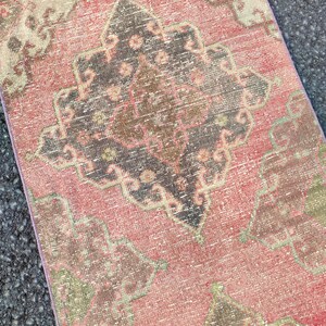 May include: A distressed, rectangular rug with a faded, vintage appearance. The rug features a central medallion design in shades of black, brown, and pink, surrounded by a pink and beige background. The rug's edges are a lighter pink.