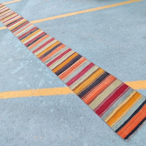 May include: A long, narrow, striped rug with a vibrant color palette. The rug features alternating bands of red, orange, yellow, black, and gray. The rug is likely made of woven fabric and is suitable for a hallway or entryway.