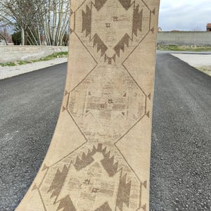 May include: A beige and brown patterned rug with geometric designs. The rug is rolled up, displaying its intricate patterns and colour palette. The rug is made of a soft material and is suitable for home decor.