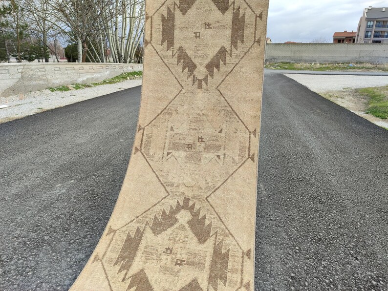 May include: A beige and brown patterned rug with geometric designs. The rug is rolled up, displaying its intricate patterns and colour palette. The rug is made of a soft material and is suitable for home decor.