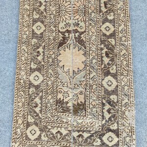 May include: A rectangular, vintage rug with a central floral design and detailed border patterns. The rug features a palette of brown, beige, and muted green tones, creating a warm aesthetic. The rug's dimensions are not visible.