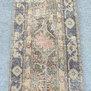 Peut inclure: Un tapis rectangulaire de style vintage avec un motif floral central dans des tons de marron, pêche et vert. Le tapis a une bordure bleu foncé avec des motifs géométriques et un aspect vieilli, suggérant qu'il s'agit d'une pièce ancienne.