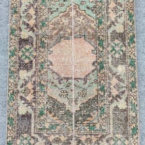 May include: A rectangular, vintage rug with a central medallion design. The rug features a palette of muted colours, including shades of green, brown, and peach. The intricate patterns and distressed appearance suggest a traditional, handcrafted origin.