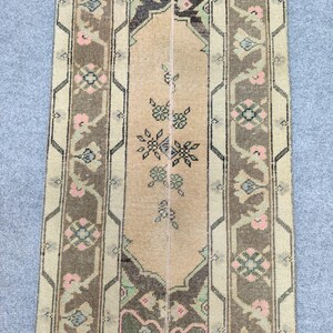 Könnte beinhalten: Ein rechteckiger Teppich im Vintage-Stil mit einem beigen Mittelteil und gemusterten Bordüren. Der Teppich weist florale und geometrische Muster in Braun-, Rosa- und Grüntönen auf und schafft eine warme Ästhetik. Geeignet für einen Flur oder Eingangsbereich.