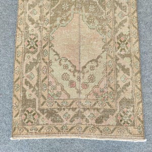 Könnte beinhalten: Ein rechteckiger Vintage-Teppich mit einem zentralen Medaillon-Design. Der Teppich hat eine gedämpfte Farbpalette aus Beige, Rosa und Olivgrün mit komplizierten floralen und geometrischen Mustern. Die Ränder des Teppichs sind leicht ausgefranst.