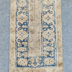 Könnte beinhalten: Ein rechteckiger Teppich mit beigem Hintergrund und einem sich wiederholenden Muster aus blauen floralen Designs. Der Teppich hat einen blauen und beigen Rand mit einem Used-Look.