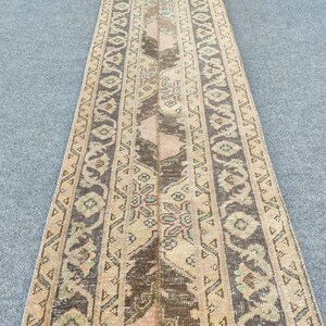 Könnte beinhalten: Ein rechteckiger Teppich im Vintage-Stil mit einer braunen Mittelbahn und gemusterten Bordüren. Der Teppich weist eine Mischung aus Beige-, Braun- und gedeckten Rosatönen mit aufwendigen geometrischen und floralen Mustern auf. Geeignet für einen Flur oder Eingangsbereich.