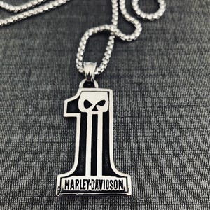 Peut inclure: Collier avec pendentif Harley-Davidson argenté. Le pendentif en forme de chiffre un, avec un motif de crâne et le logo Harley-Davidson en bas. La chaîne est une chaîne gourmette argentée.