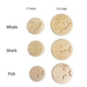 May include: A collection of round wooden stamps featuring engraved marine animal designs. The set includes whale, shark, and fish motifs in two sizes: 2 inches labeled Small and 2.5 inches labeled Large, arranged in a grid with text labels.