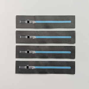 May include: Four rectangular patches with a dark gray background, each featuring a light blue lightsaber design. The lightsabers have a silver handle and a bright blue blade. The patches are arranged in a vertical stack.