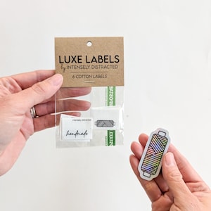 May include: A package of six cotton labels with the text "LUXE LABELS by INTENSELY DISTRACTED" on the front. The package includes two labels with the text "handmade" and a holographic sticker of a spool of thread.