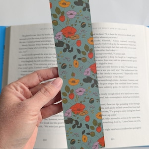 May include: A teal blue bookmark with a floral pattern featuring red, orange, yellow, and purple flowers. The flowers are surrounded by green leaves and small white dots.