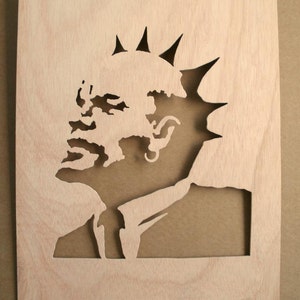 May include: A wooden stencil of a person's face with a mohawk hairstyle. The stencil is cut out of a light brown piece of wood.