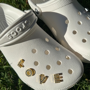 May include: White Crocs with the word "LOVE" spelled out in gold letters with rhinestones.