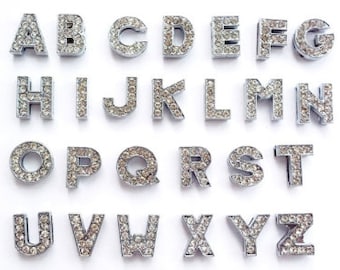 May include: A set of 26 silver-toned alphabet letter charms, each adorned with clear rhinestones. The letters are arranged in alphabetical order.