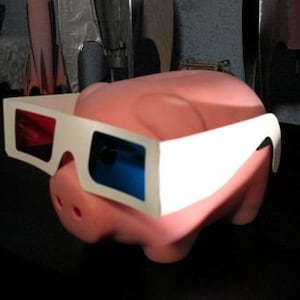 May include: A pink piggy bank wearing white 3D glasses with red and blue lenses.