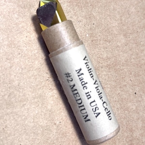 May include: A small cardboard tube with a gold and black rosin stick inside. The tube is labeled "Violin-Viola-Cello Made in USA #2 MEDIUM".