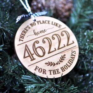 May include: A round wooden ornament with the text "There's no place like home" and the number "4622" in a decorative font. The ornament also has the text "For the Holidays" and a small sprig of greenery with berries.