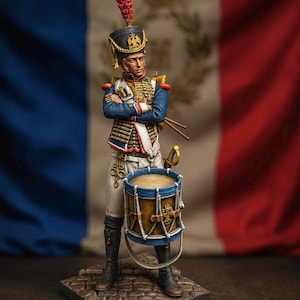 May include: A detailed miniature figurine of a Napoleonic-era drummer standing with arms crossed. The figure wears a blue uniform with gold accents, a tall shako with a red plume, and white trousers. A wooden drum with blue rims is positioned in front.