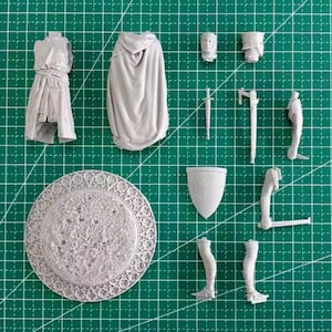 May include: A light gray resin model kit consisting of a torso, a hooded cloak, a head, a shield, a sword, and various limb components. The set includes a circular base with a textured surface and an intricate, decorative border pattern.