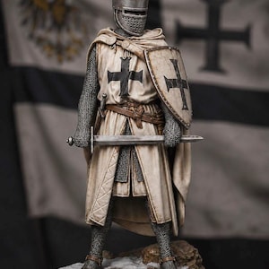 May include: A detailed figurine of a medieval knight wearing a flat-topped helmet, chainmail armor, and a cream-colored surcoat with a black cross. The knight holds a metal sword and a shield with a black cross, standing on a rocky, snow-dusted base.