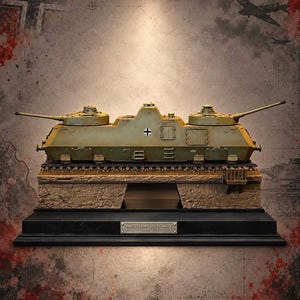 May include: A scale model of a Panzerkampfwagen Maus tank featuring a dual-turret design in olive green paint. The model sits on a textured stone-like base with a black display plinth and a metal plaque reading Panzerkampfwagen Maus Sd.Kfz. 205.