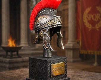 May include: A detailed replica of a Roman Empire helmet, featuring a vibrant red crest and intricate gold-colored detailing. The helmet is mounted on a black, textured base with a gold plaque that reads "Roman Empire". The background suggests an ancient Roman setting.