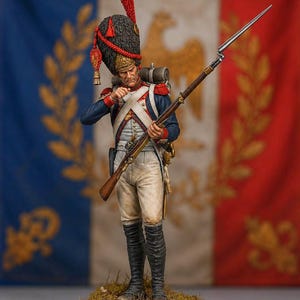May include: A detailed miniature figurine of a Napoleonic soldier wearing a tall black bearskin hat with a red plume, a blue coat with red accents, white trousers, and black boots. The soldier holds a long musket with a bayonet attached.
