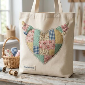 May include: Cream-colored tote bag with a patchwork heart design featuring wings. The heart is made of various patterned fabrics in pink, blue, and yellow, with a lace trim. The bag has sturdy handles and a small label that reads "bluebasketful".