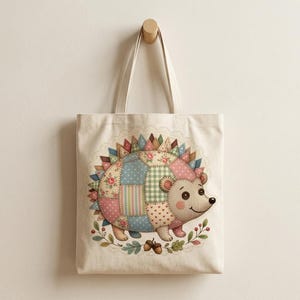 Könnte beinhalten: Eine cremefarbene Tragetasche mit einem Patchwork-Igel-Design. Der Igel hat einen farbenfrohen Patchwork-Körper mit Blumen-, Tupfen- und Streifenmustern. Das Design ist von einem floralen Kranz mit Eicheln umgeben.