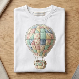 Könnte beinhalten: Weißes T-Shirt mit einem bunten Heißluftballon-Design. Der Ballon besteht aus Patchwork-Stoff in Pastellfarben und floralen Mustern. Das T-Shirt hat den Text "bluebasketful" auf dem Etikett.