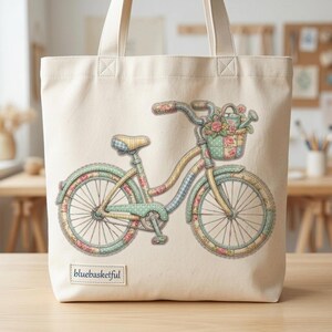 Könnte beinhalten: Cremefarbene Tragetasche mit einem skurrilen Fahrrad-Design. Das Fahrrad ist mit floralen Mustern, Pastellfarben und einem Korb voller Blumen verziert. Der Text "bluebasketful" befindet sich unten.