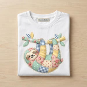 May include: White crew neck t-shirt featuring a colorful patchwork sloth design. The sloth is hanging from a branch with floral and gingham patterns. The design includes pink, blue, yellow, and green colors. The brand name "bluebasketful" is visible on the collar.