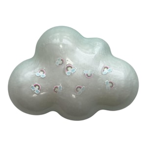 Peut inclure: Objet décoratif en forme de nuage blanc nacré. De petits autocollants arc-en-ciel sont dispersés sur la surface. L'objet a une finition lisse et brillante et un design fantaisiste.