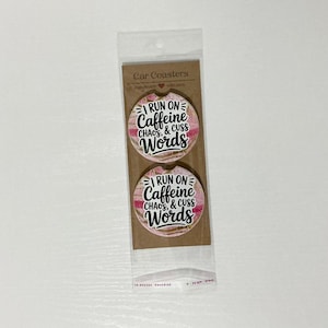 May include: Two car coasters with a pink and white striped background. The coasters have the text "I RUN ON Caffeine, CHAOS, & CUSS Words" in black and white. The coasters are packaged in a clear plastic sleeve.