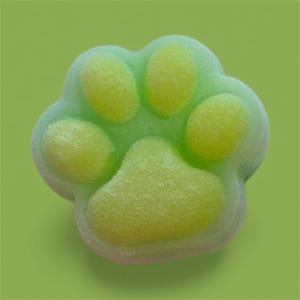 Könnte beinhalten: Ein grün-gelbes pfotenförmiges Objekt, möglicherweise eine Badekugel oder Seife, vor einem einfarbigen grünen Hintergrund. Der Pfotenabdruck hat ein strukturiertes Aussehen mit abgerundeten Ballen in einer helleren gelben Farbe.