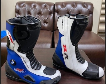 Puede incluir: Par de botas de moto azules, blancas y negras. Las botas tienen el logotipo de BMW Motorrad y la marca RR. Las botas son de cuero y tienen un diseño protector.