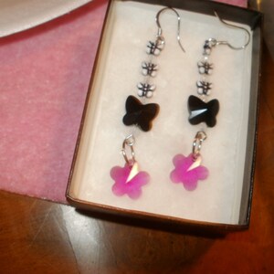 May include: A pair of earrings with black butterfly charms and pink flower accents. The earrings are hanging from silver hooks.