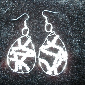 May include: A pair of white beaded earrings with a silver wire frame. The earrings are shaped like teardrops and have a delicate, intricate design.