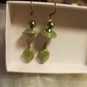 May include: A pair of green button earrings with green glass beads and gold-toned metal accents.