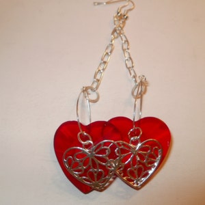 May include: A pair of red heart-shaped earrings with silver filigree designs. The earrings are suspended from a silver chain.
