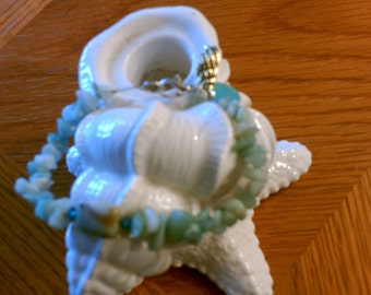 May include: A white ceramic seashell with a light blue and green gemstone bracelet wrapped around it.