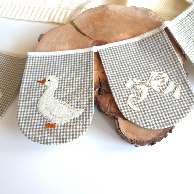 Handmade white goose garland displayed above crib, alternating orange wavy-edged ovals with felt geese in blue hats, baby room banner, goose nursery decor, cotton bunting.