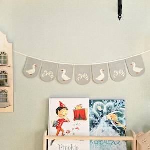 Close-up of cotton bunting flags featuring white geese with tiny blue pom-pom hats on orange wavy ovals, nursery wall decoration, kids room garland, handmade goose nursery decor.