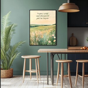 May include: A framed art print featuring a field of wildflowers under a yellow sky. The artwork includes the text "To grow: a child must feel accepted just as they are." The print is displayed in a kitchen setting with wooden stools and a plant.
